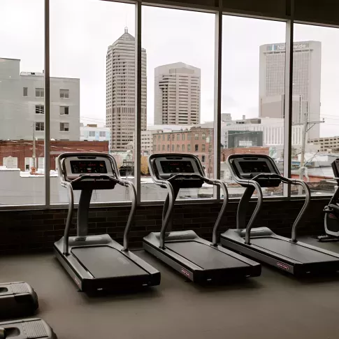 Treadmills in a modern apartment fitness center with large floor-to-ceiling windows overlooking the downtown Columbus skyline.