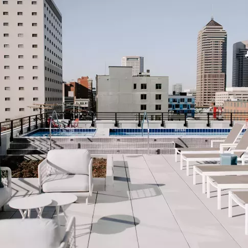 Rooftop pool and sundeck with lounge chairs and modern outdoor seating overlooking the downtown Columbus skyline at an urban apartment community.