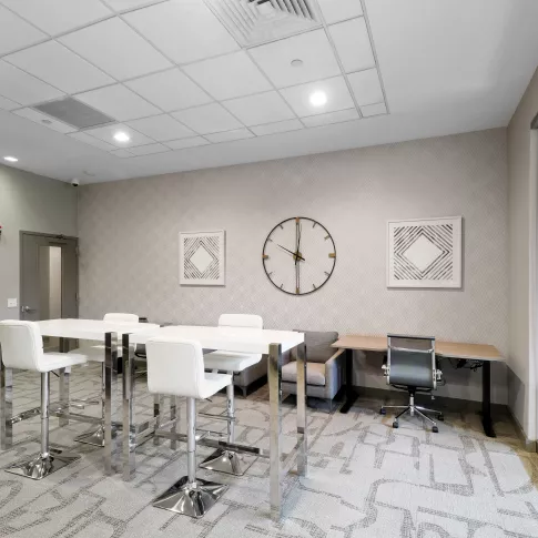 The resident business center includes communal high-top tables for coworking and a glass-enclosed meeting space.