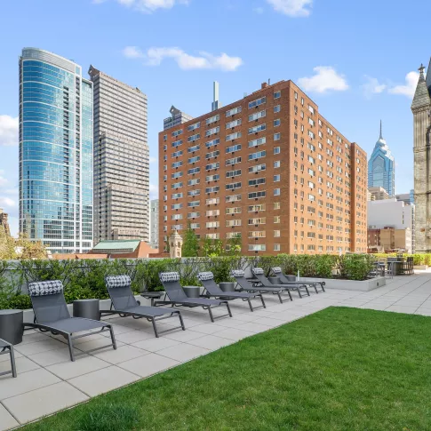 Outdoor lounge area featuring modern chaise lounges, decorative pillows, and lush green lawn with city views.