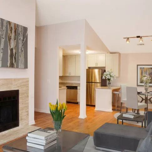 Modern living room with gray sofa, stone fireplace, birch tree painting, and open-plan kitchen and dining area.