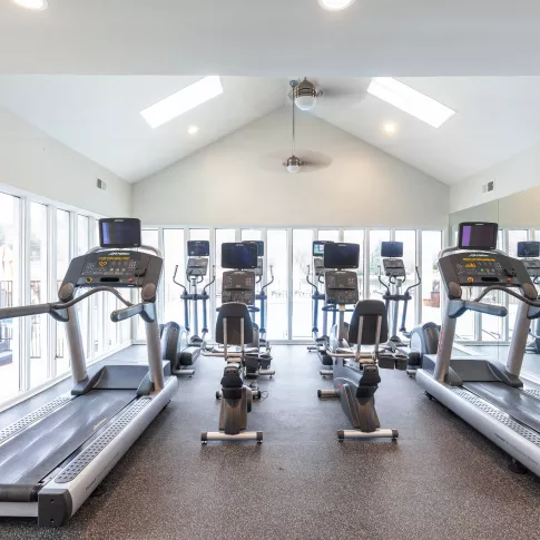 Bright fitness center at Hillmeade Apartments with treadmills and ellipticals facing floor-to-ceiling windows. The cardio area offers views of the outdoor pool deck.