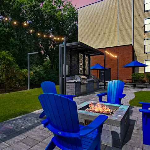 Outdoor fire pit with blue seating chairs at Riverbend on the Charles apartment community.