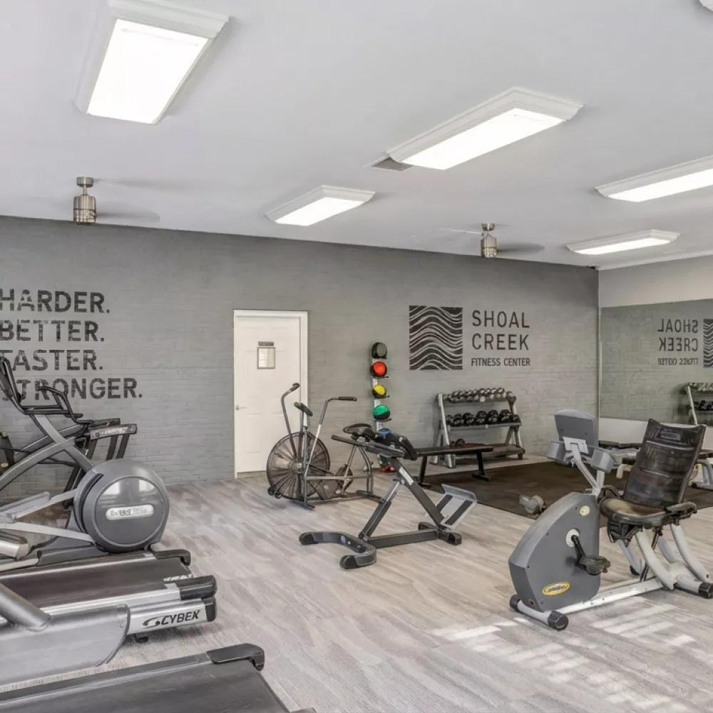 Spacious, well-lit gym featuring treadmills, ellipticals, stationary bikes, weights, and motivational wall text.
