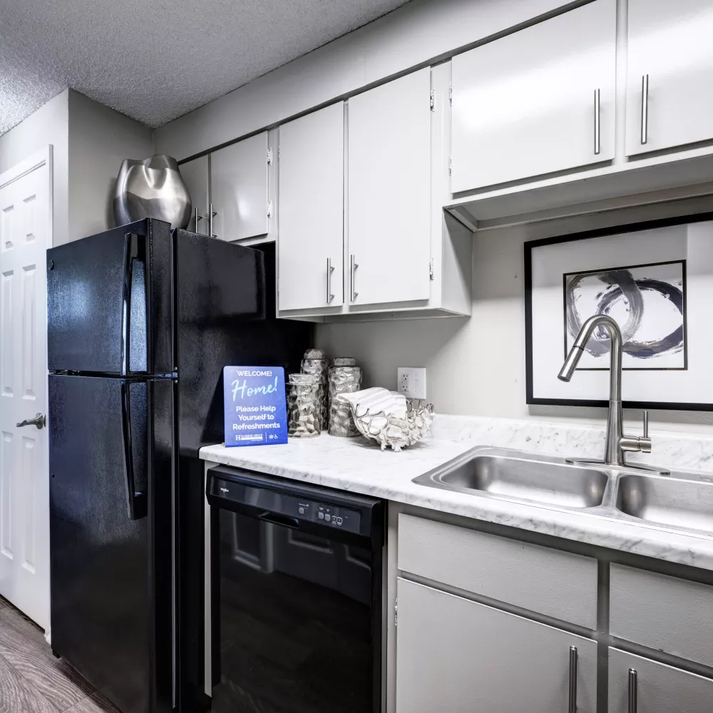 Modern kitchen with light grey cabinets, white speckled counters, black appliances, stainless steel sink, and abstract art.