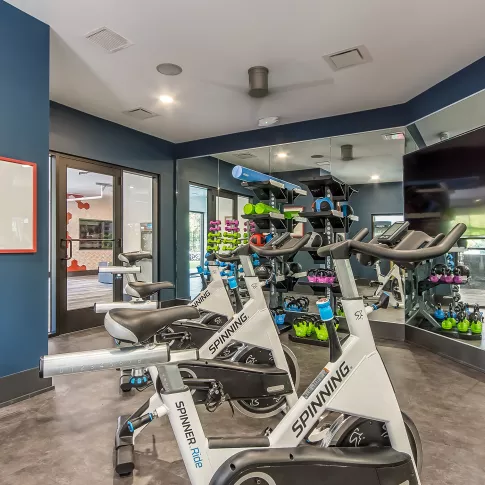 Indoor cycling studio featuring white and blue spin bikes, a mirrored wall with TV, and dark blue accent walls.