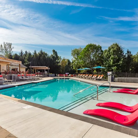 Spacious outdoor swimming pool with turquoise water, red submerged lounge chairs, and poolside seating under a blue sky.