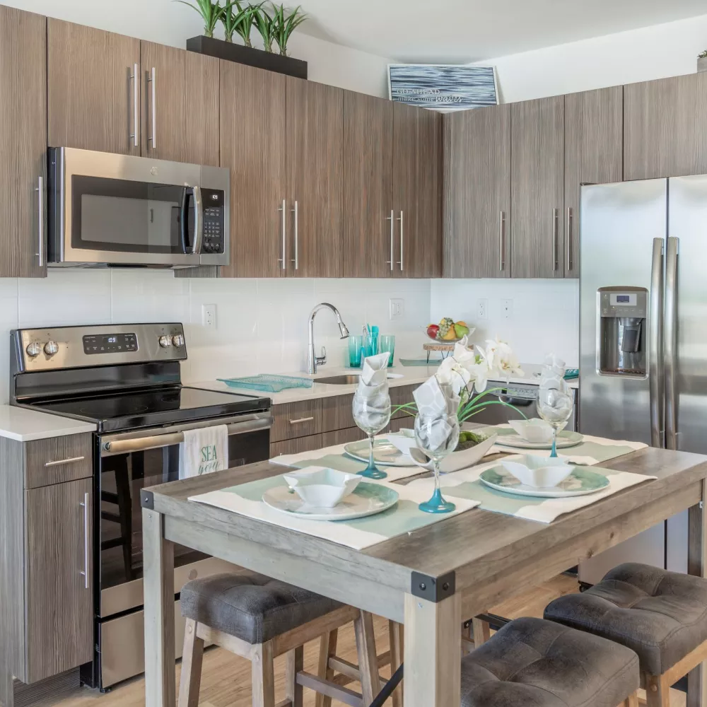 Modern kitchen with wood cabinets, stainless steel appliances, and an island set for dining. Potted plants add greenery.