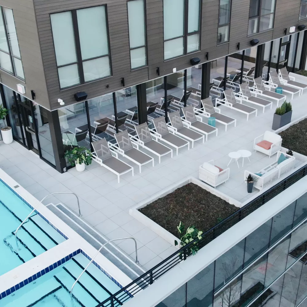 Modern rooftop pool deck with a clear blue swimming pool, rows of grey lounge chairs, and white seating areas.