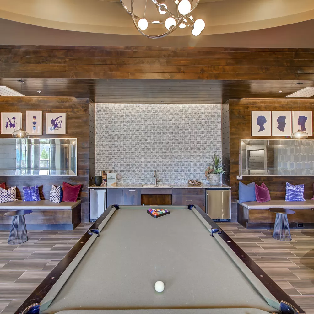 Modern common room with a pool table, wooden walls, mosaic backsplash, and diverse seating areas with colorful cushions.