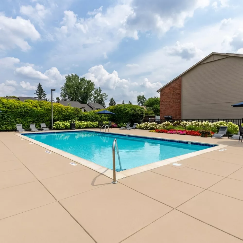Photograph of an outdoor swimming pool area with blue water, lounge chairs, blue umbrellas, green landscaping, and a brick building.