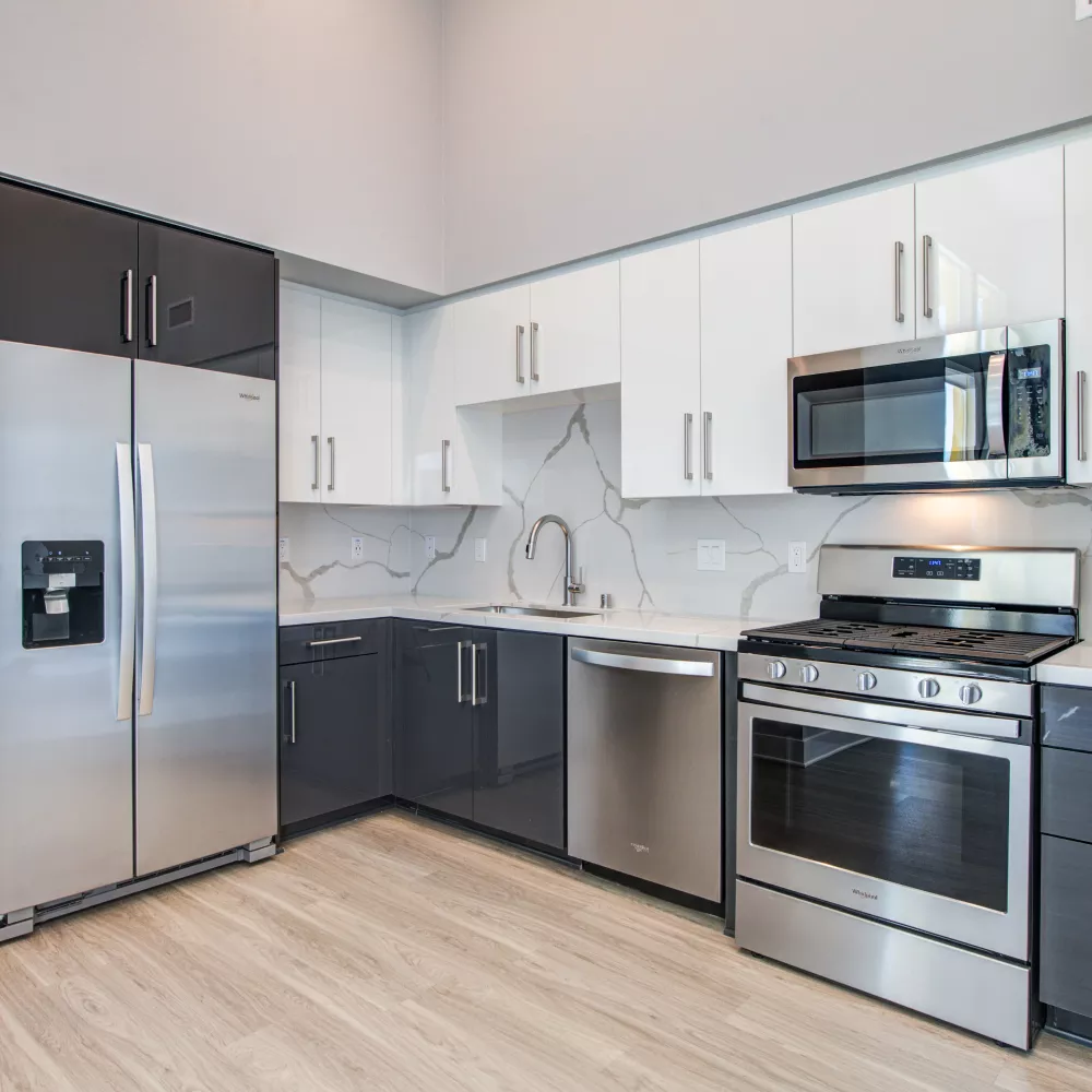 Modern kitchen with dark gray and white cabinets, stainless steel appliances, marble-look countertops, and wood floors.