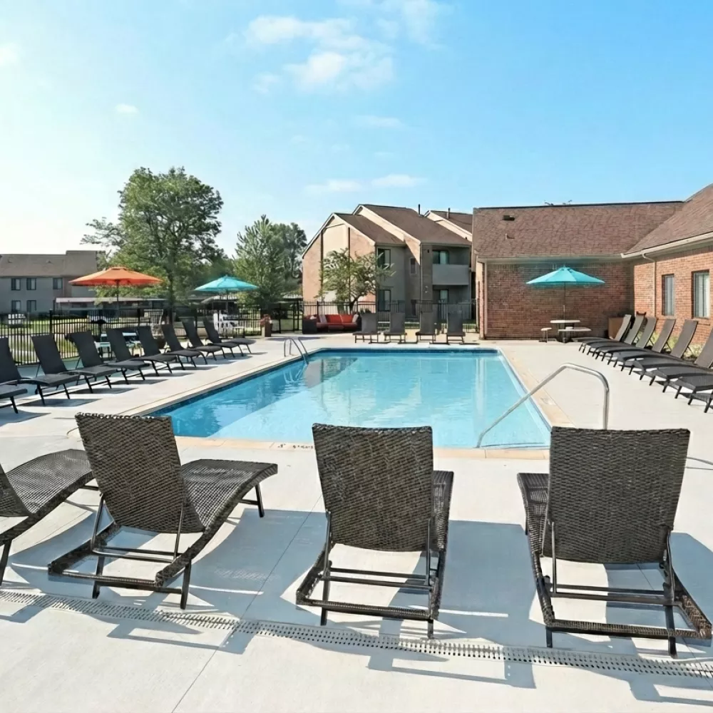 Outdoor swimming pool with many lounge chairs, surrounded by brick apartment buildings under a blue sky.