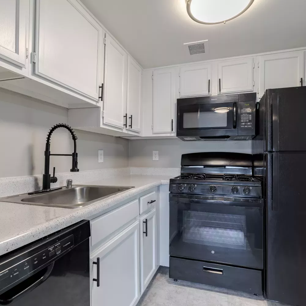 Clean kitchen featuring white flat-panel cabinets, light gray counters, black appliances, and a stainless steel sink.