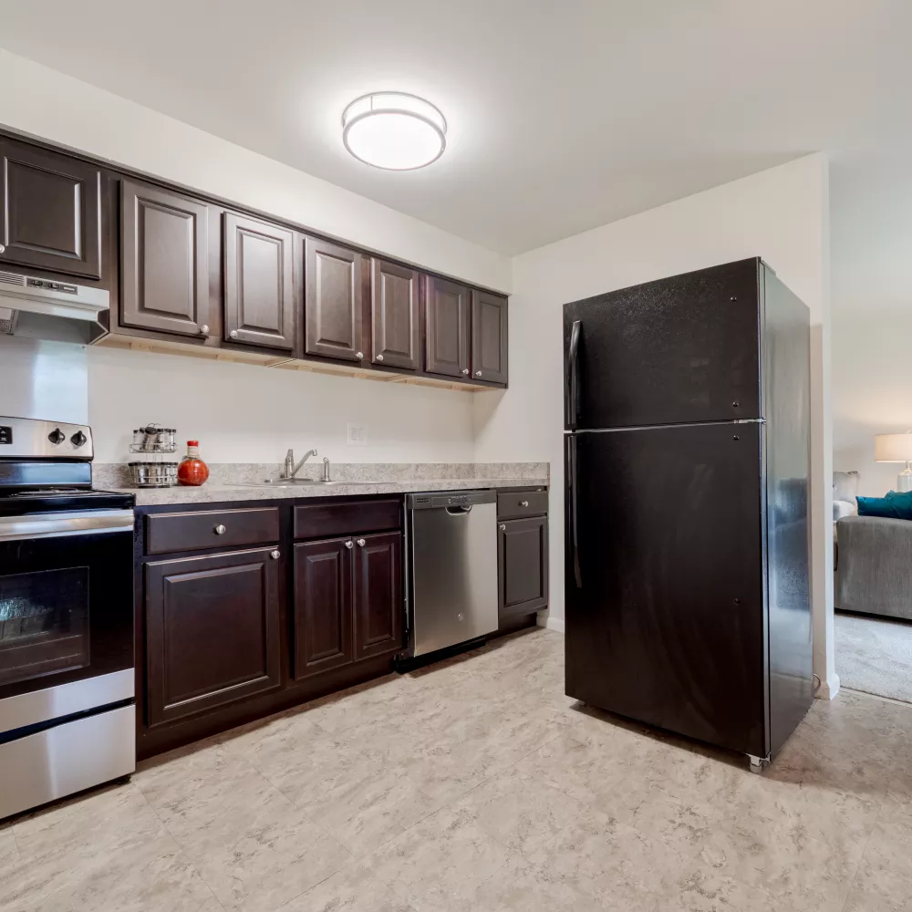 Modern kitchen with dark cabinets, stainless steel appliances, black fridge, and a red kettle. Living room visible beyond.