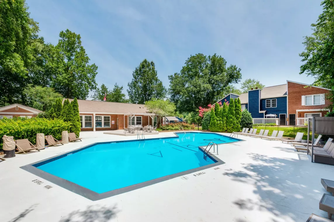 "Outdoor pool area surrounded by lounge chairs, lush greenery, and charming residential buildings."