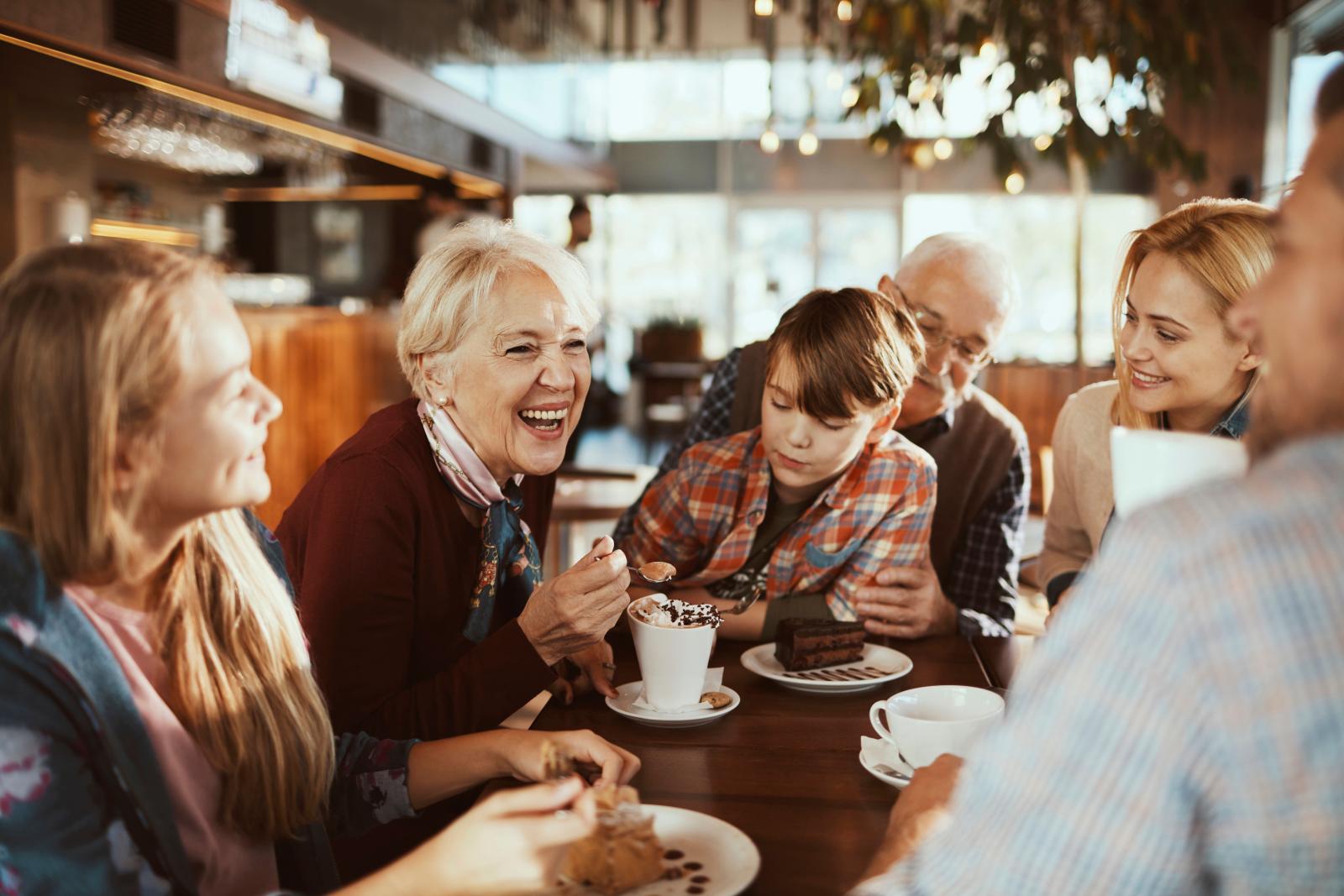 A joyful group of people of various ages gathers around a table, enjoying desserts and drinks in a warm, inviting café.