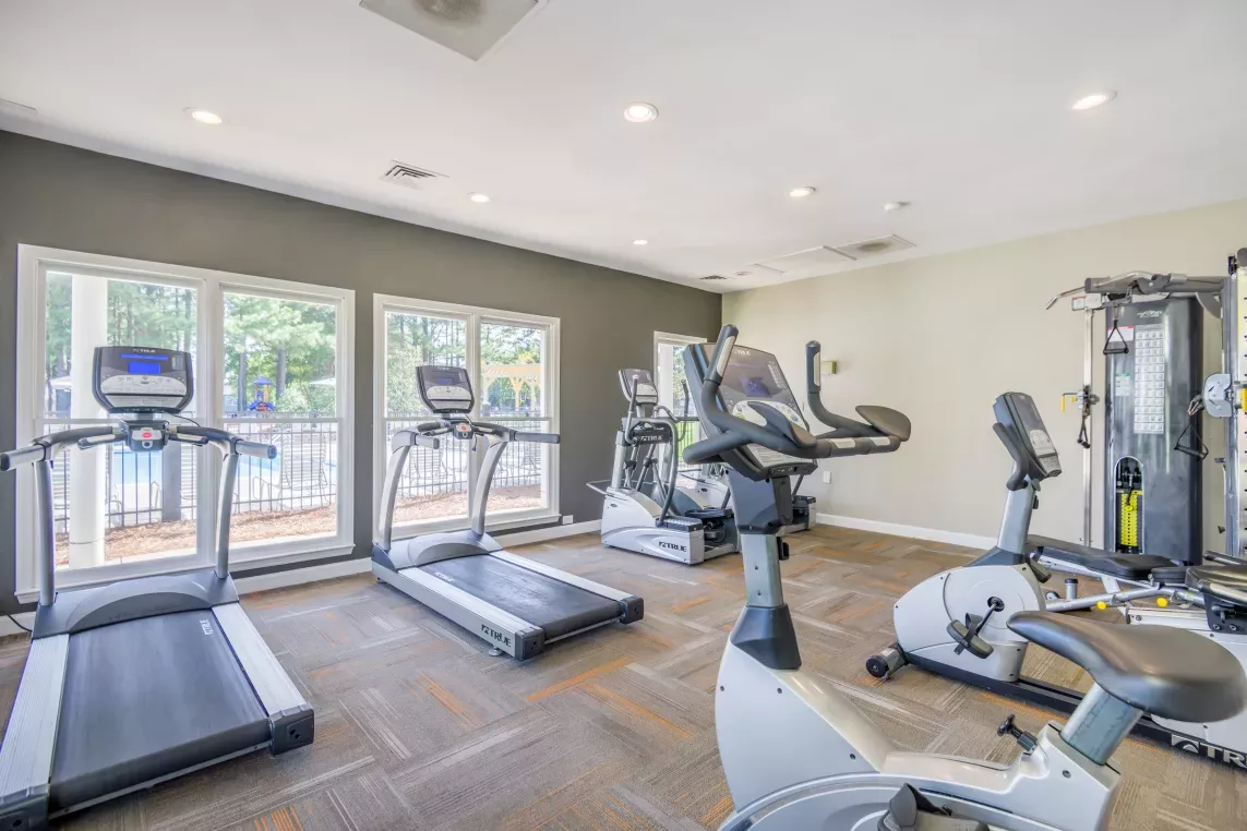  A well-lit fitness center featuring treadmills, stationary bikes, and strength training equipment with large windows overlooking outdoor greenery.