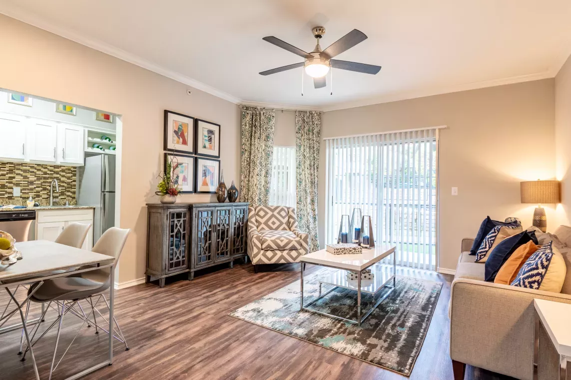 A modern and stylish living room with a ceiling fan, colorful decor, and a view of the dining area and kitchen.