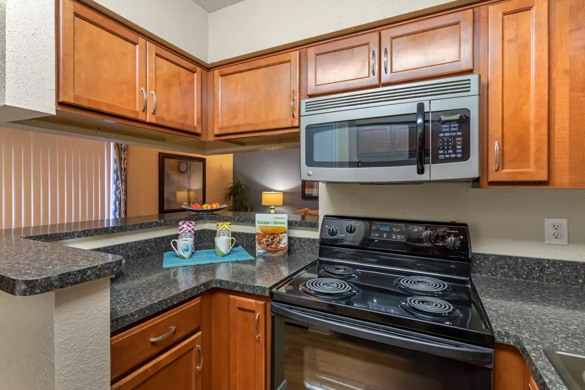 Modern kitchen featuring rich wood cabinetry, black appliances including a gas stove and microwave, and sleek countertops. The space is well-lit and functional, with a cozy bar area for added convenience and style.