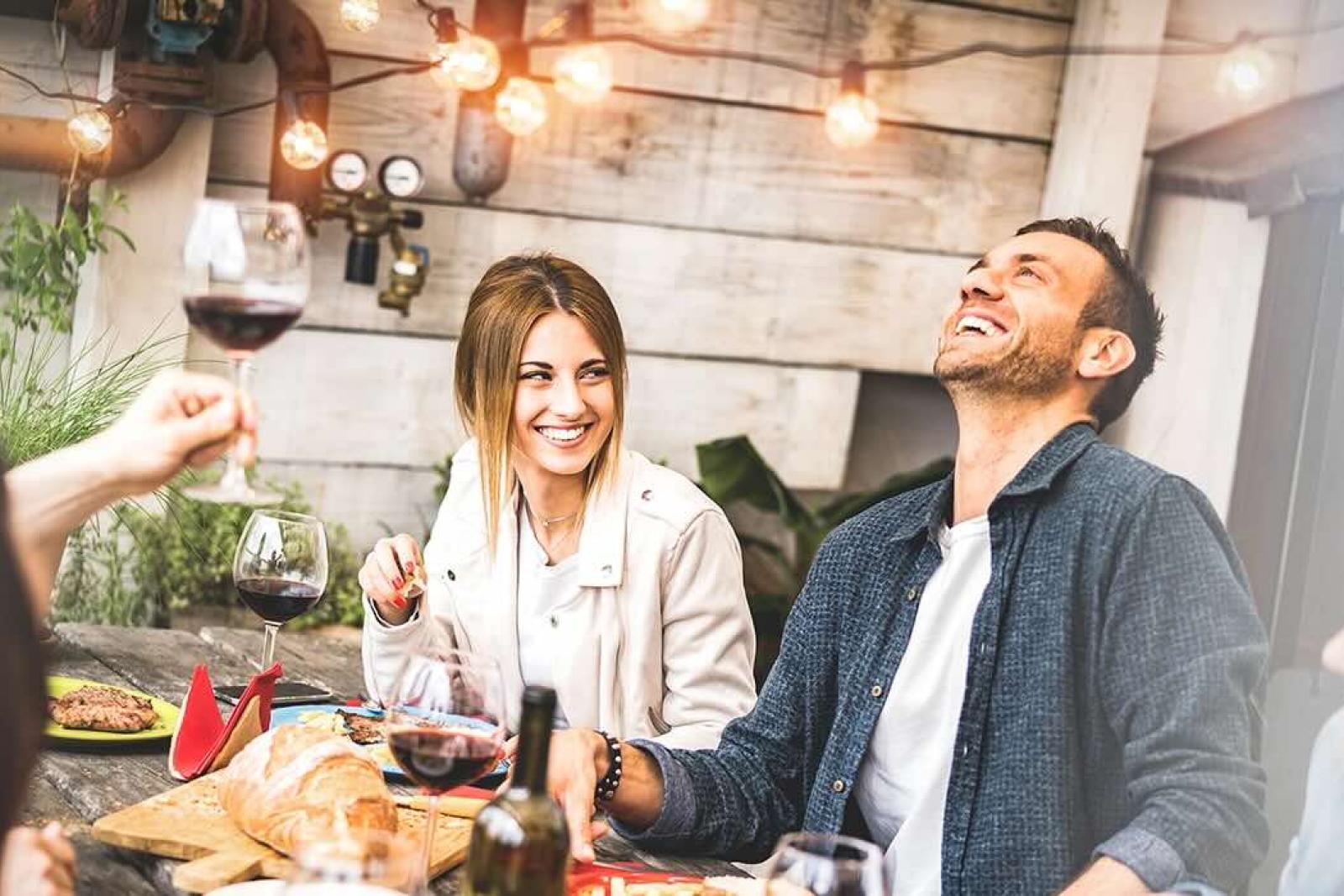 A group of friends enjoying food, wine, and laughter at a cozy outdoor gathering.