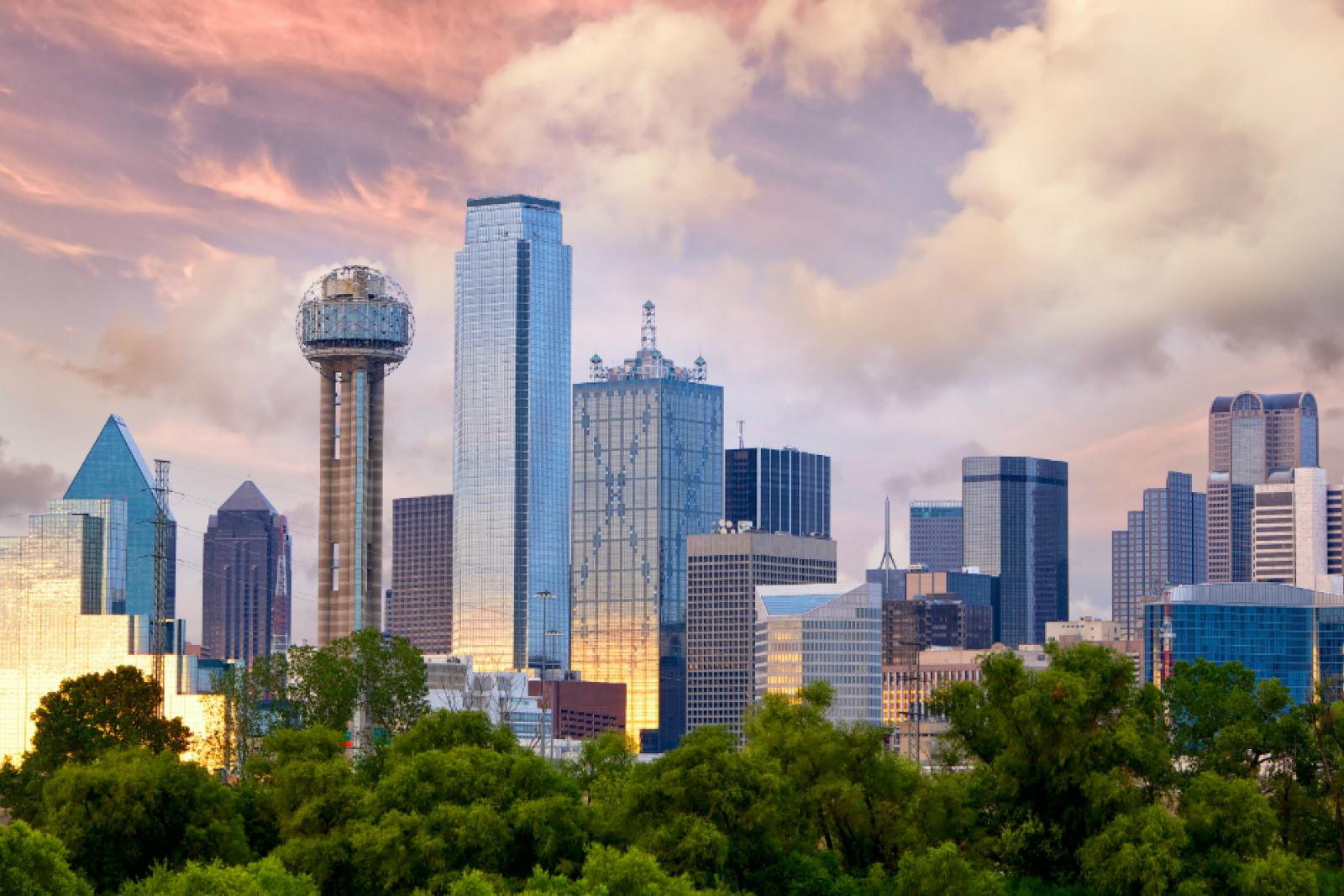 A scenic view of Lewisville, Texas, featuring a vibrant skyline with lush greenery in the foreground and dramatic clouds during sunset.