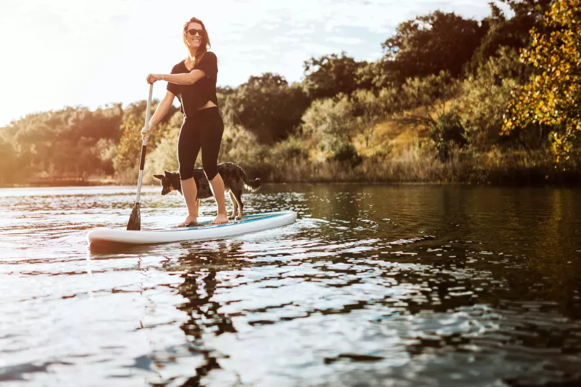 A woman paddleboarding on a serene lake with her dog, enjoying the outdoors.