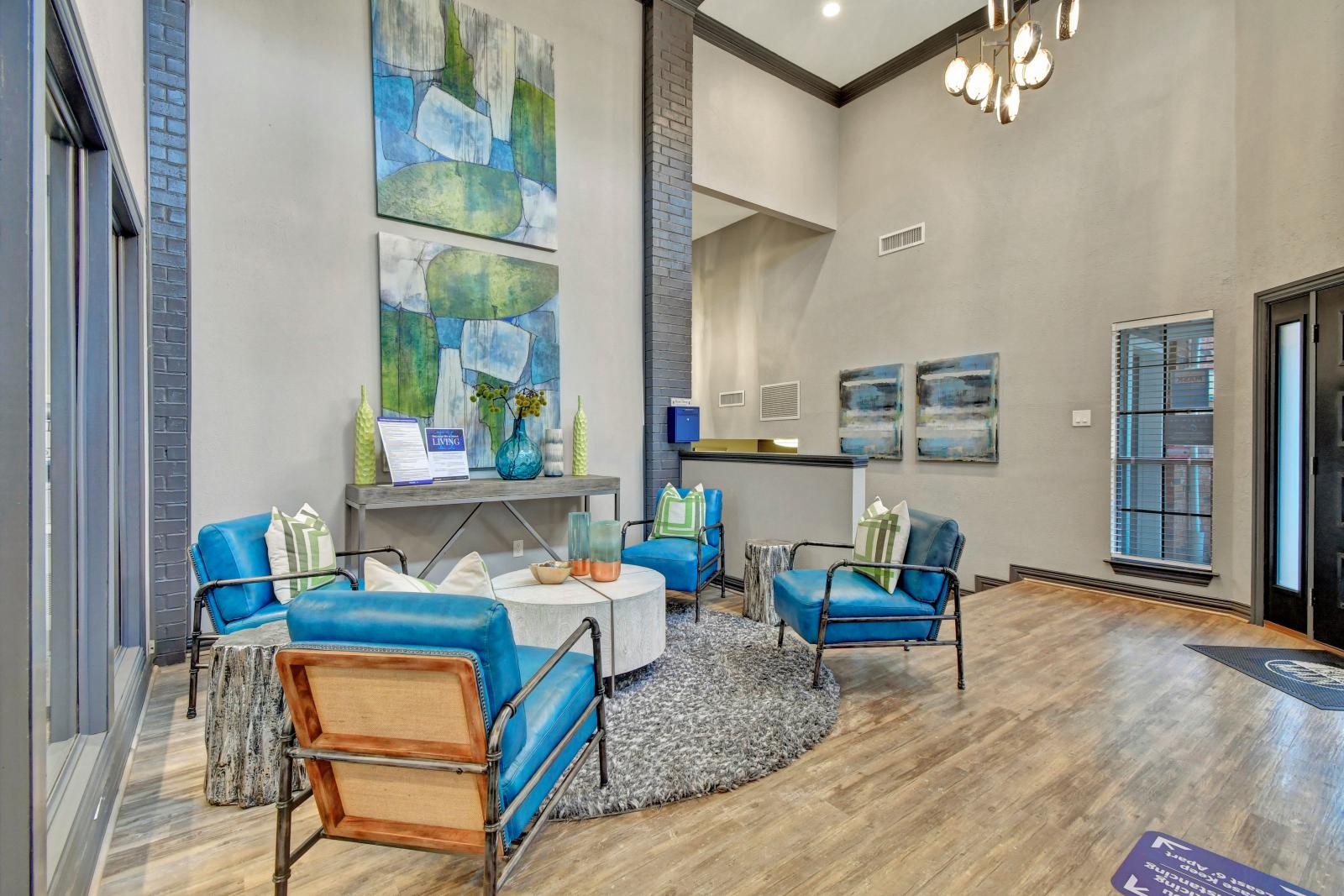 A modern and stylish lounge area featuring blue accent chairs, contemporary artwork, and a cozy round rug in a bright, open space.