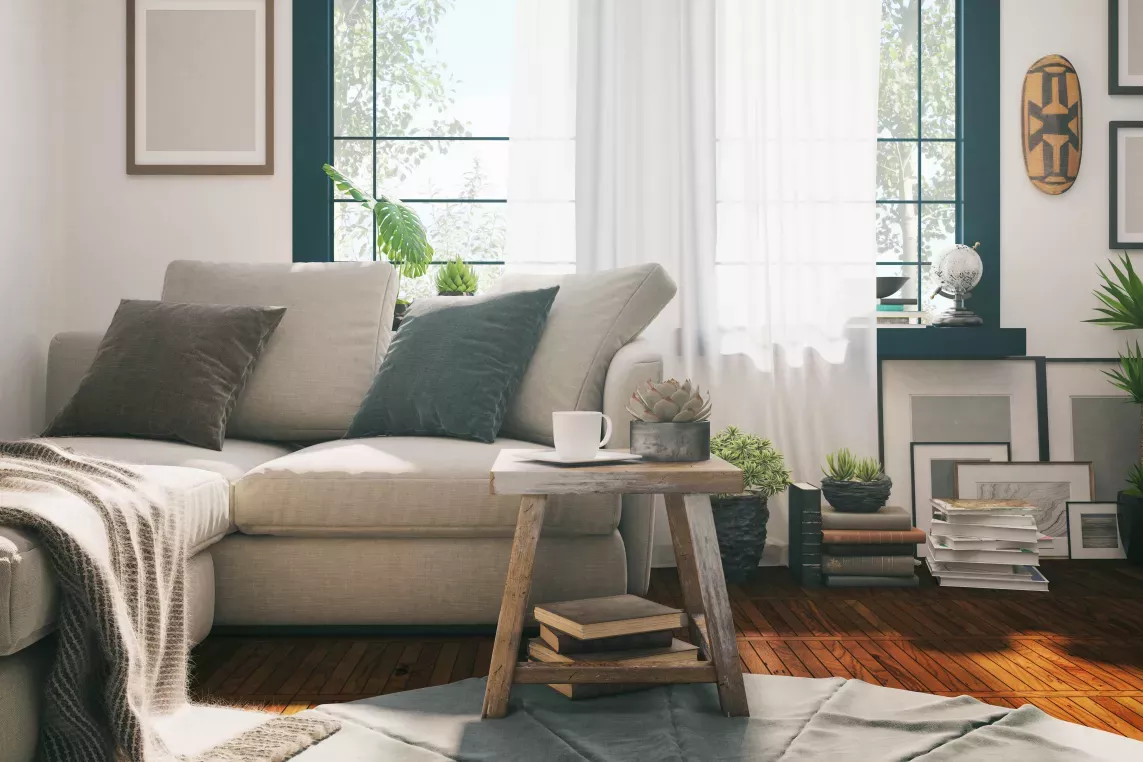 A cozy living room with a light beige sectional sofa, a wooden coffee table, and abundant natural light streaming through large windows adorned with sheer white curtains.