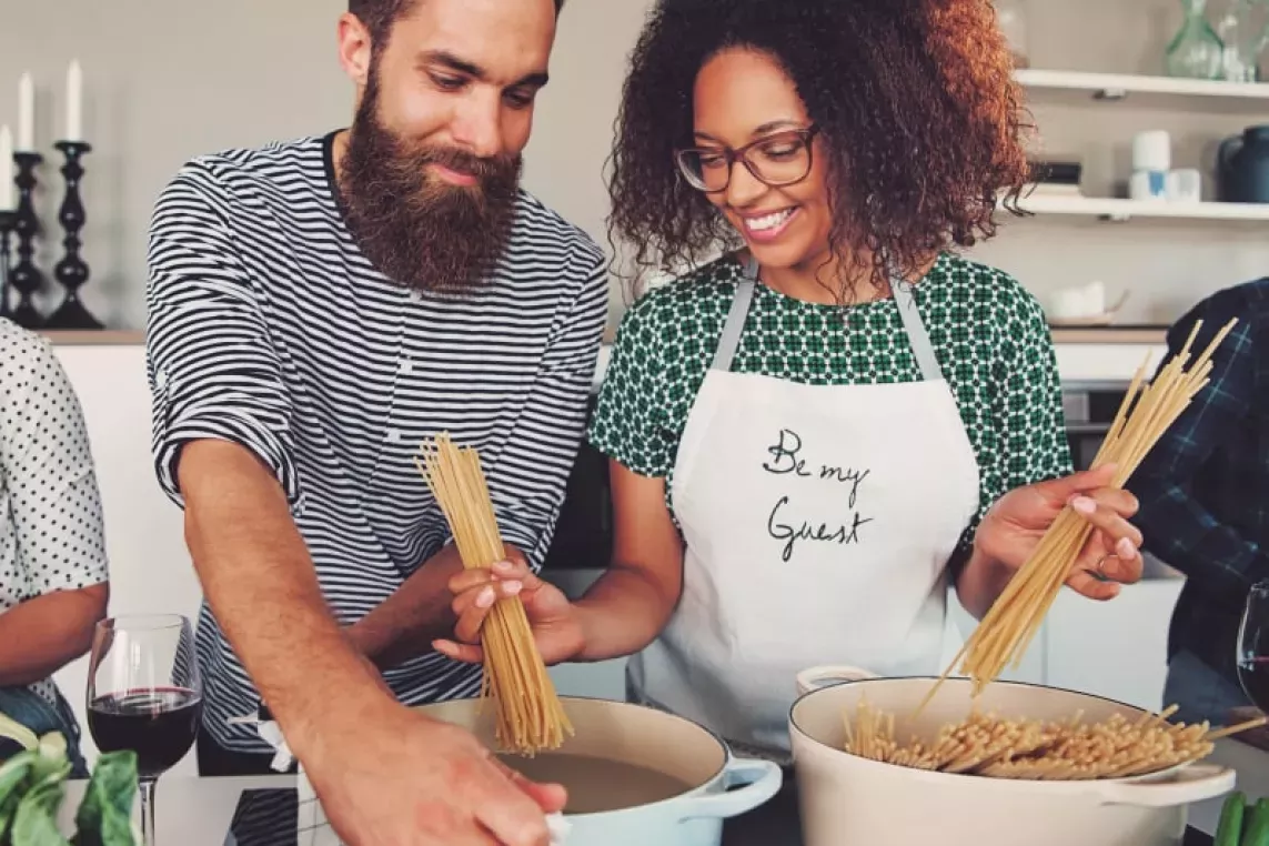 Couple happily cooking together in the kitchen, preparing pasta with smiles and teamwork, creating a warm and inviting atmosphere for home cooking and shared moments.