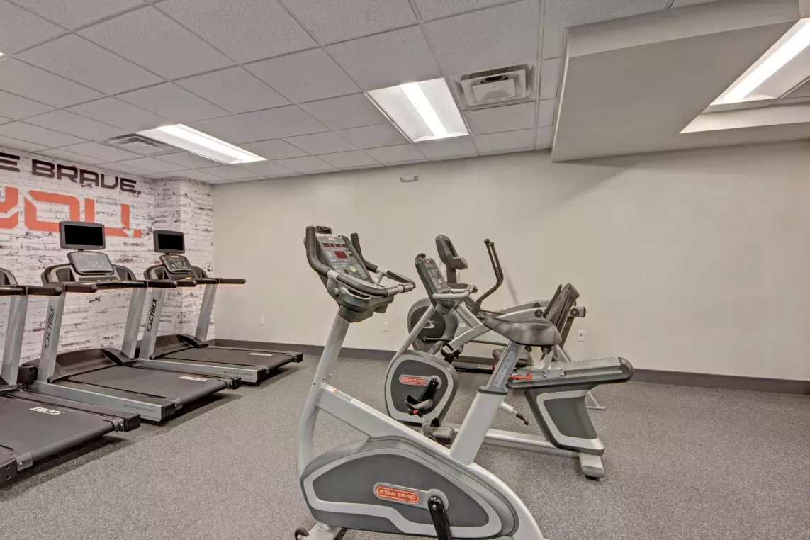 A fitness center with stationary bikes and treadmills arranged under bright overhead lighting.