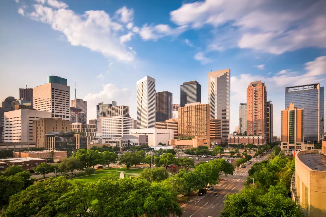 A scenic city skyline showcasing modern skyscrapers, a lush green park, and a bright blue sky with wispy clouds.