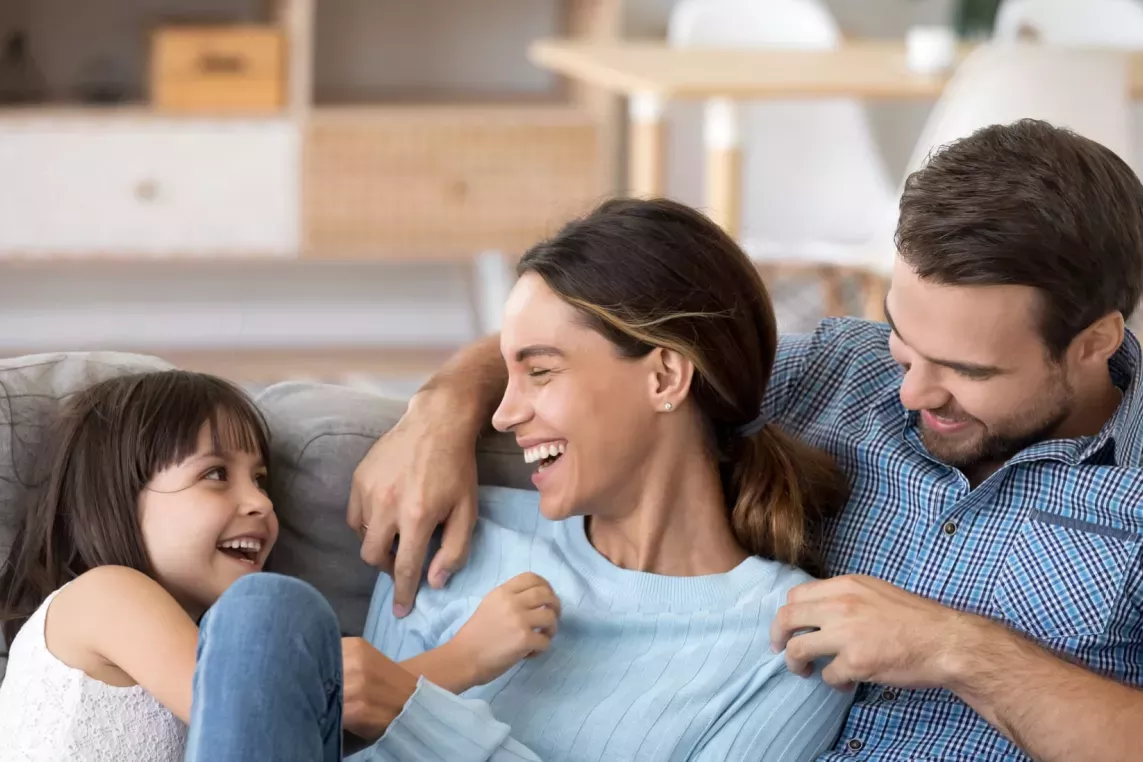 Happy family sitting together on a cozy couch, sharing smiles and laughter, creating a warm and joyful atmosphere in a comfortable home setting.