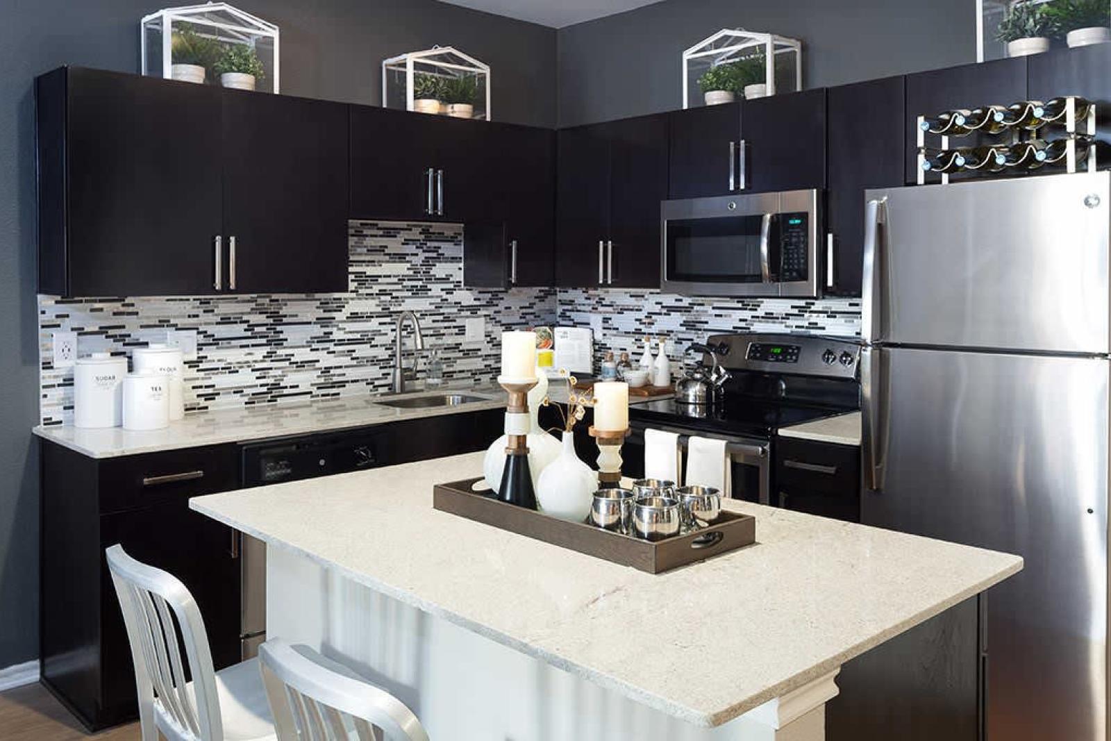 Modern kitchen with dark cabinets, stainless steel appliances, and a decorative backsplash, featuring a white island with stools.