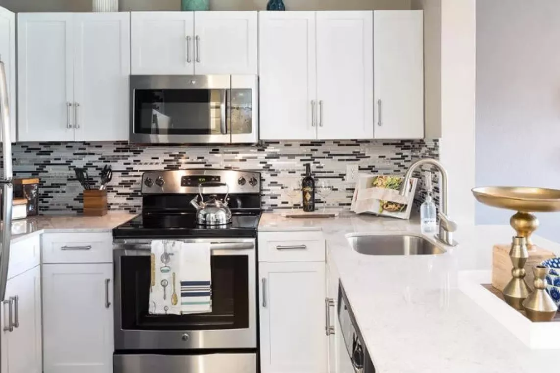 A modern kitchen with stainless steel appliances, white cabinetry, a mosaic tile backsplash, and a sleek countertop featuring decorative accents and a gold centerpiece.