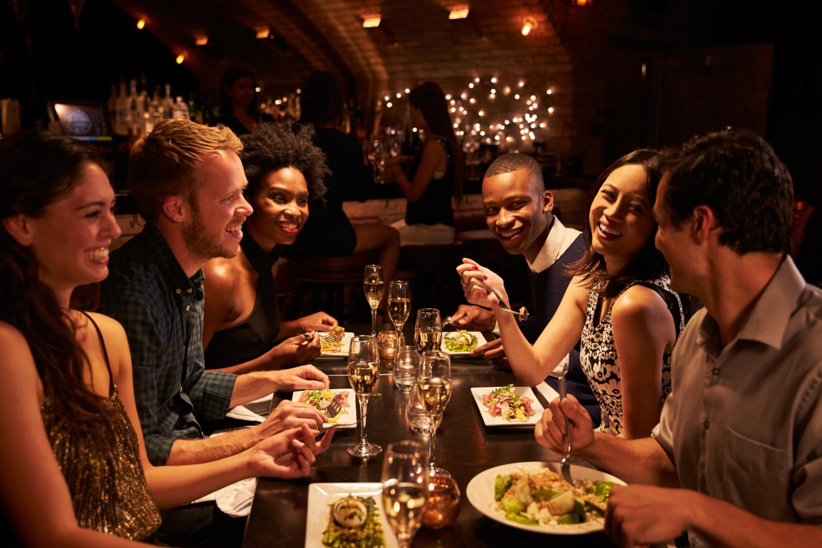 A group of friends enjoying a meal together at a cozy, dimly lit restaurant, showcasing the vibrant social opportunities and dining experiences available near the apartment community.