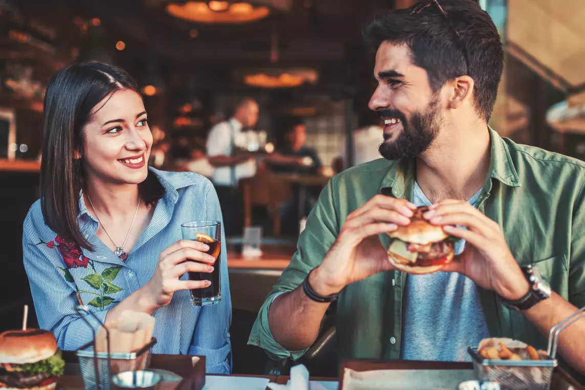A couple enjoying a casual meal together at a restaurant, smiling and engaging in conversation over burgers and drinks.