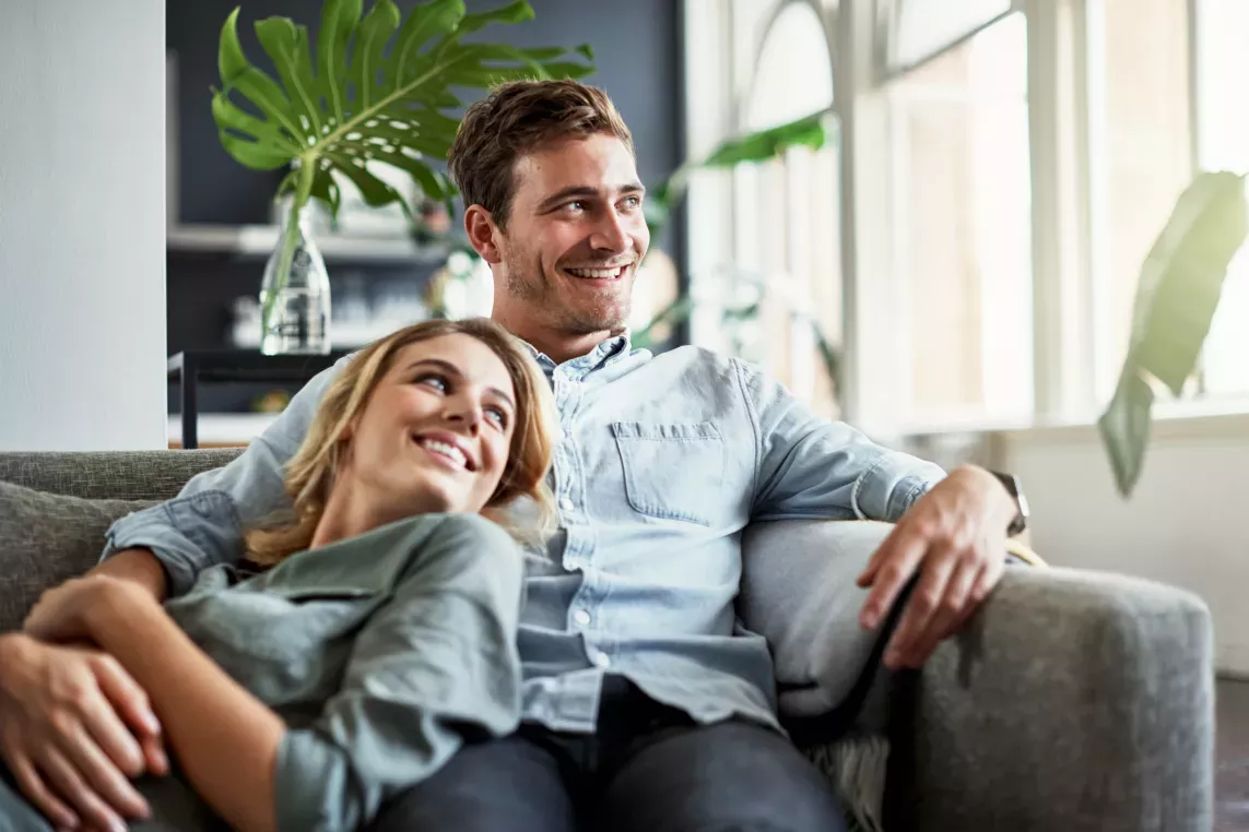 A happy couple relaxes on a comfortable sofa in a bright and stylish living room, surrounded by greenery and natural light.