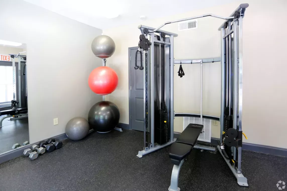 A fully equipped fitness center at Norcross Crossings Apartments featuring modern exercise machines, free weights, and yoga balls, with large windows providing natural light.