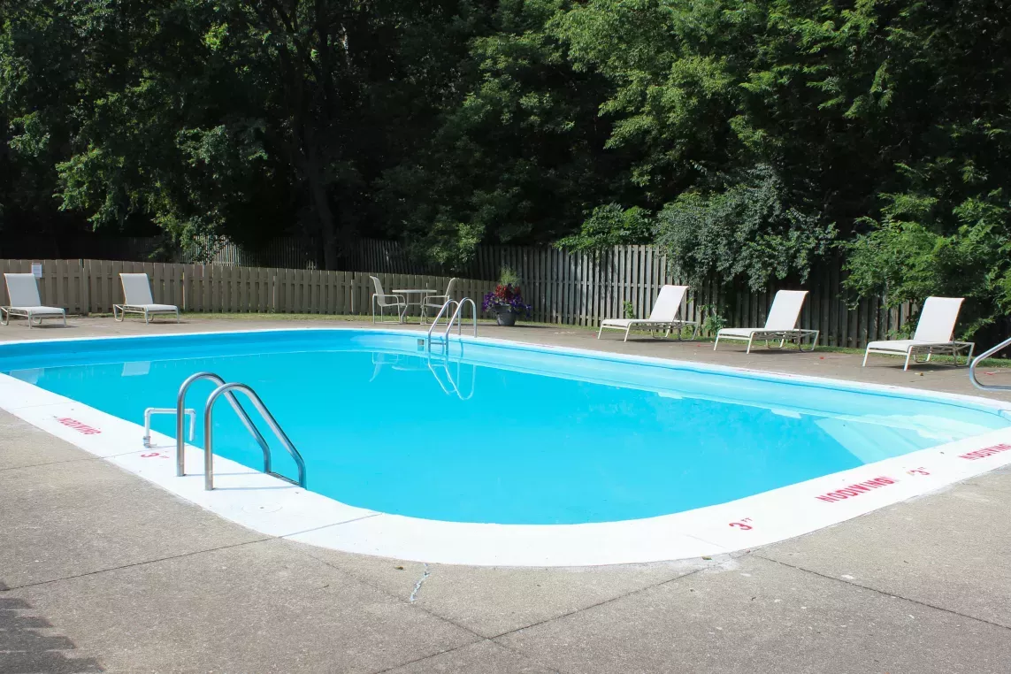 The outdoor pool area at North River Place Apartments, surrounded by lounge chairs, fencing, and trees, offers a refreshing retreat for residents
