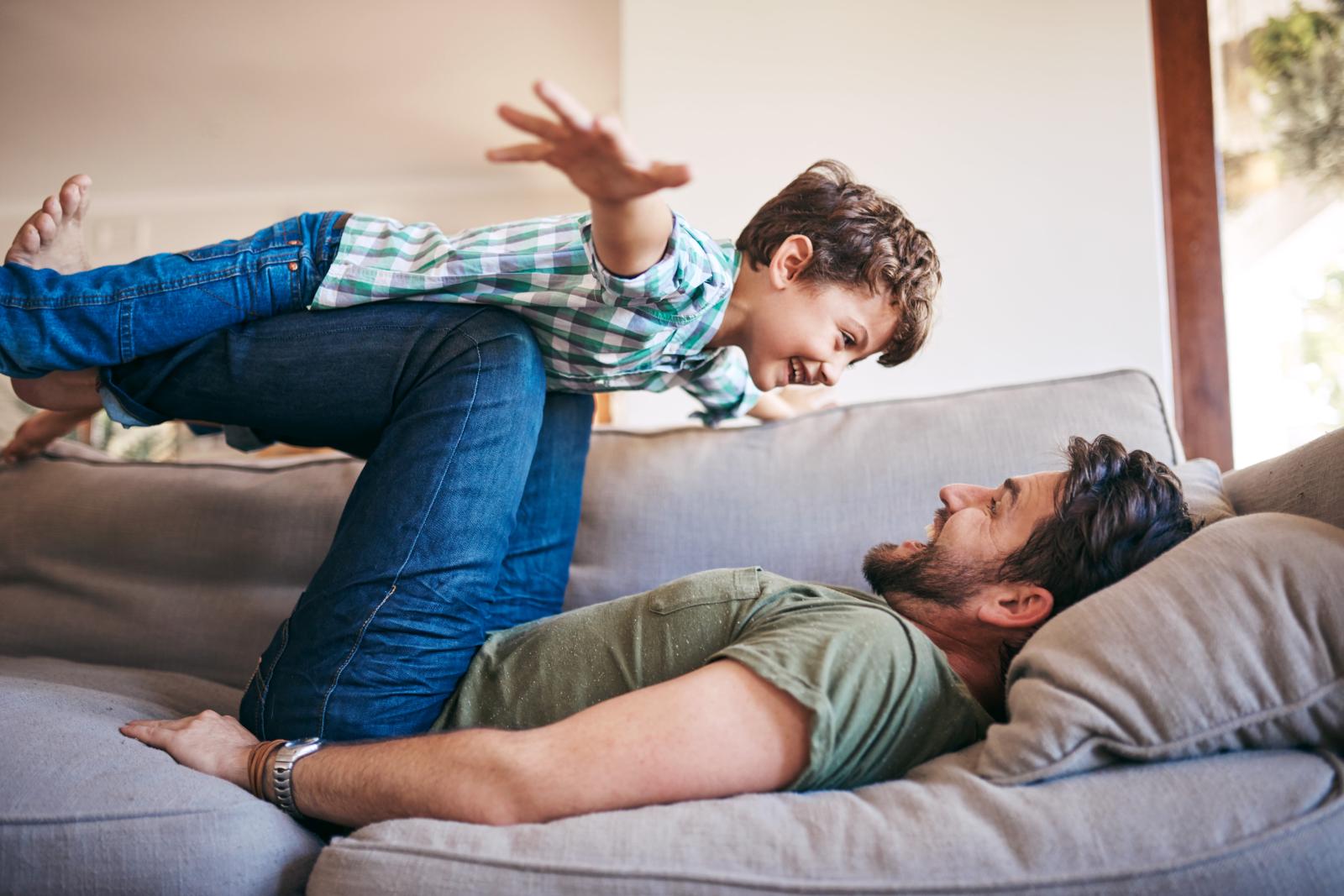 A father and his young son playing together on a couch, filled with joy and laughter.
