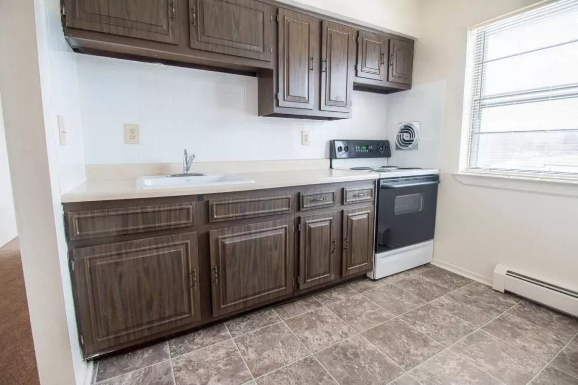 Kitchen area at Washington Gardens Apartments in Washington, NJ, featuring dark wood cabinetry, a single sink, a stove, and a large window allowing natural light.
