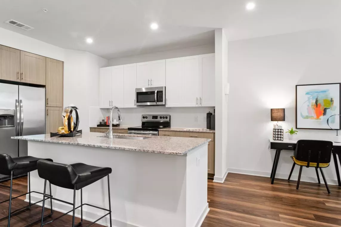 A modern kitchen with stainless steel appliances, white cabinetry, and a granite countertop with barstools.