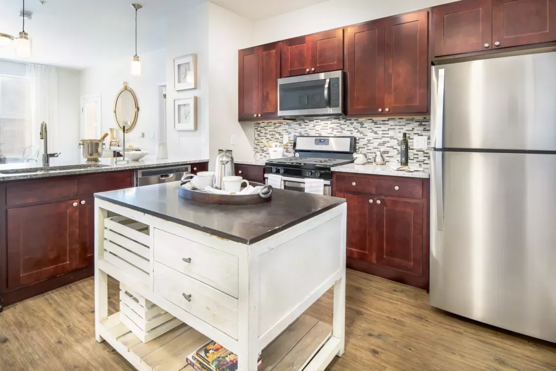 A modern kitchen at The Royal Belmont Luxury Apartments featuring stainless steel appliances, granite countertops, cherry wood cabinets, and a stylish central island.