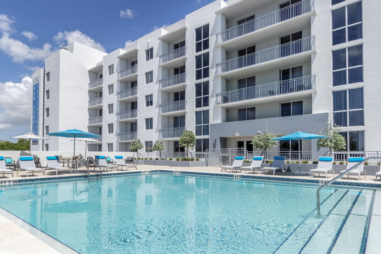 Resort-style pool area at 275 Fontaine Parc Luxury Apartments with sparkling blue water, sun loungers, and contemporary white building facade in the background.
