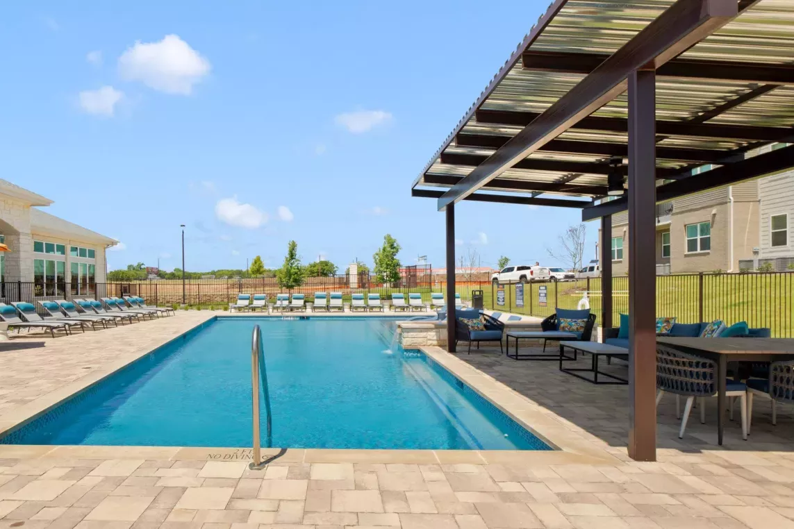 Outdoor swimming pool with lounge chairs and a shaded seating area.
