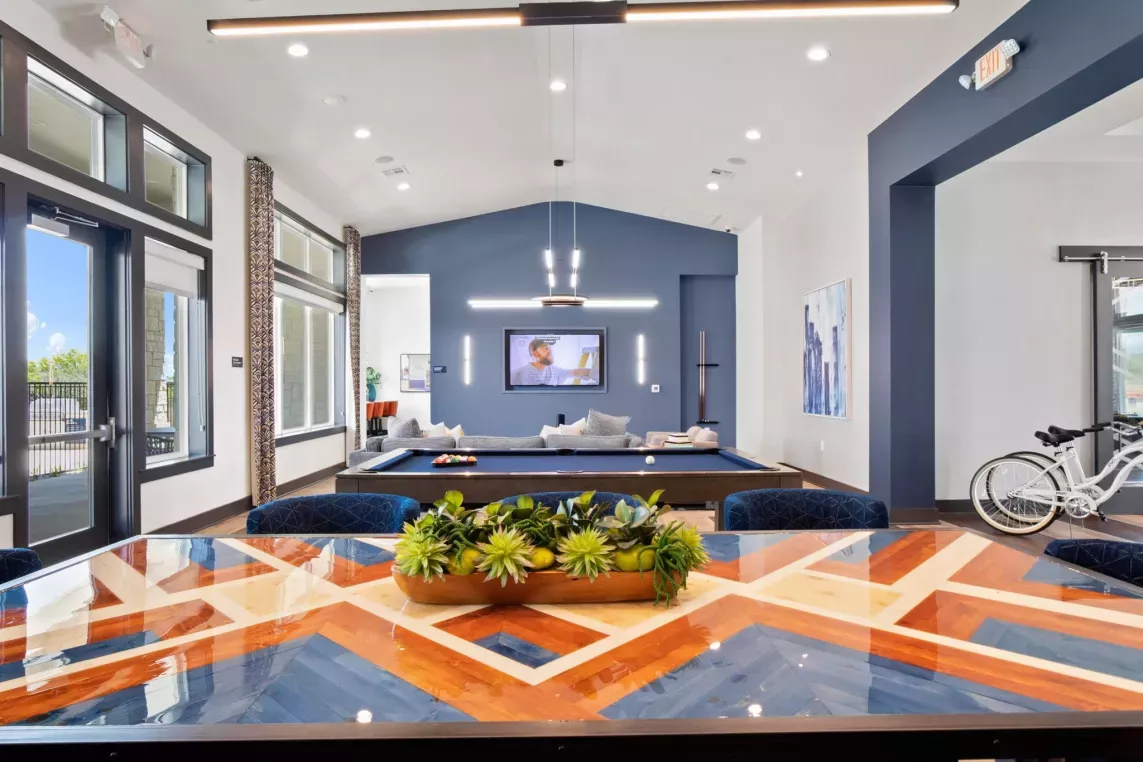 A bright community lounge with a colorful geometric dining table and a pool table in the background.