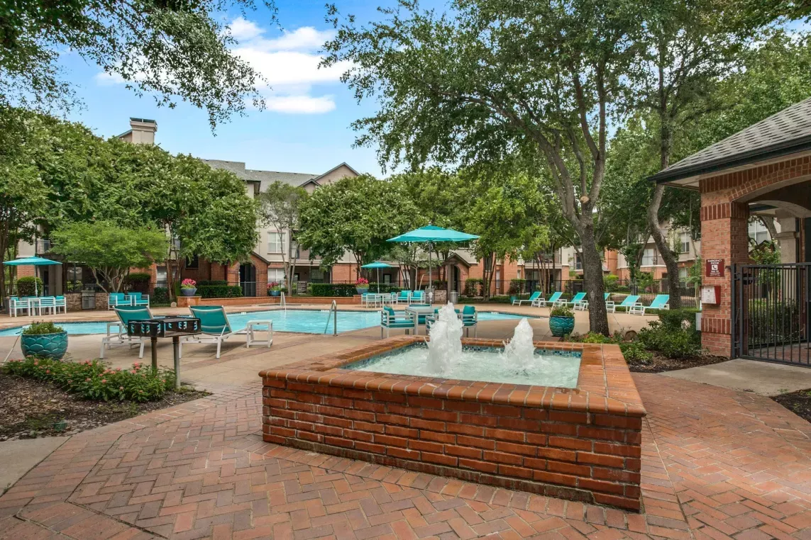 A serene courtyard with a bubbling fountain, landscaped pathways, and views of the swimming pool.