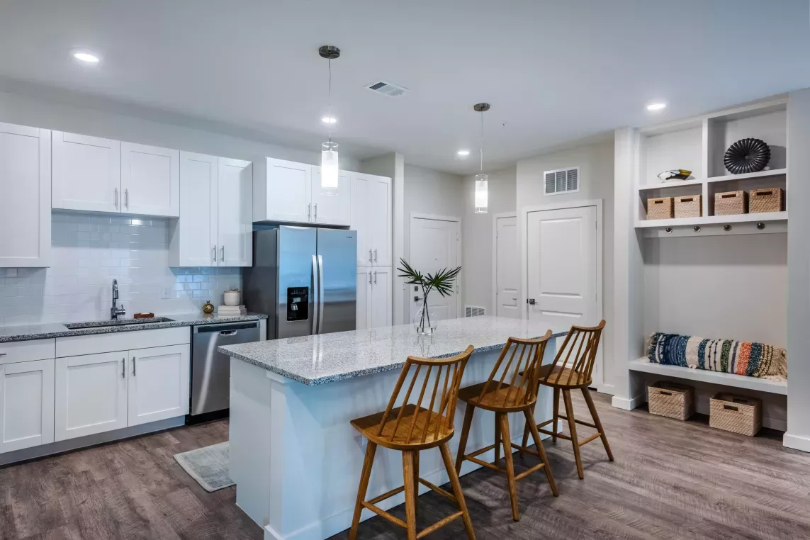 A modern kitchen featuring white cabinetry, stainless steel appliances, granite countertops, and pendant lighting over a spacious island with wooden barstools.