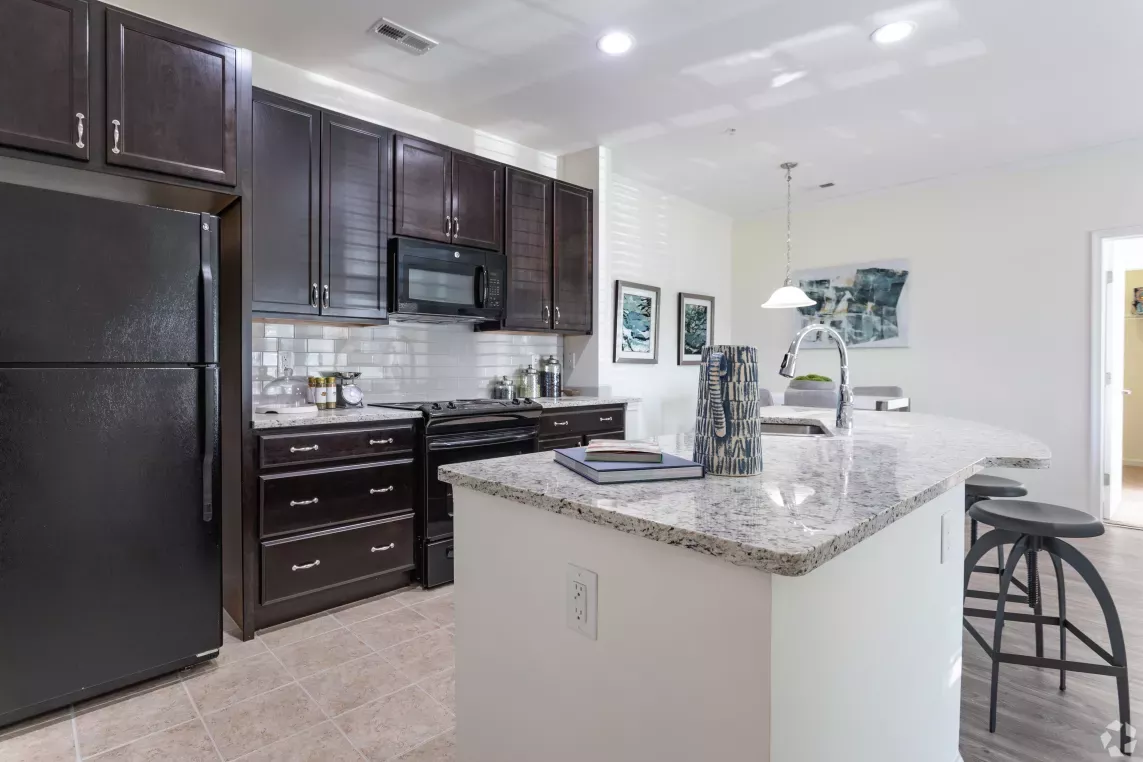 A sleek kitchen featuring dark wood cabinets, a granite countertop, and a breakfast bar with stools under pendant lights.